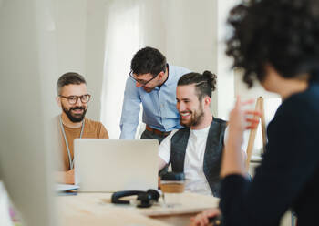 Eine Gruppe junger, fröhlicher Geschäftsleute mit Laptop arbeitet in einem modernen Büro zusammen. - HPIF27865