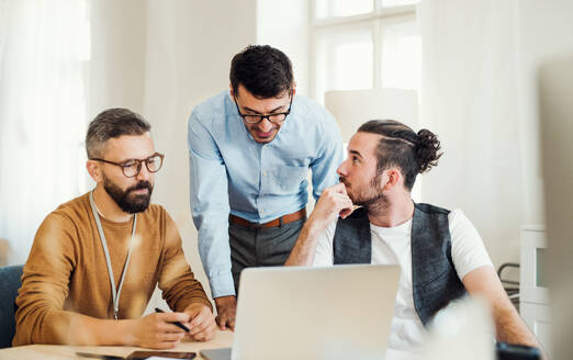 Eine Gruppe junger, konzentrierter männlicher und weiblicher Geschäftsleute mit Laptop arbeitet in einem modernen Büro zusammen. - HPIF27866