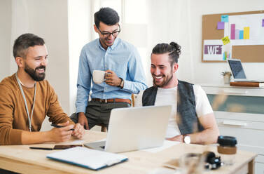 Gruppe von jungen, fröhlichen Geschäftsleuten mit Laptop, die in einem modernen Büro arbeiten. - HPIF27868