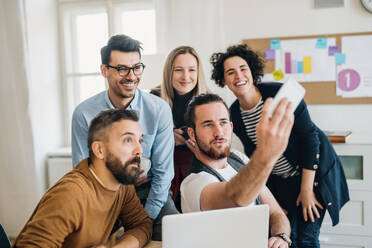 Group of young,cheerful, male and female businesspeople with smartphone in a modern office, taking selfie. - HPIF27871