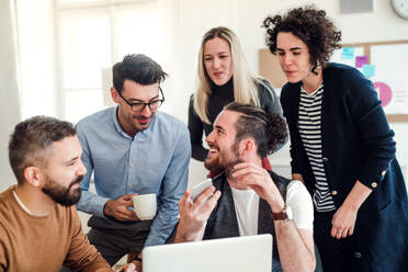 Eine Gruppe junger, fröhlicher Geschäftsleute mit Laptop arbeitet in einem modernen Büro zusammen. - HPIF27872