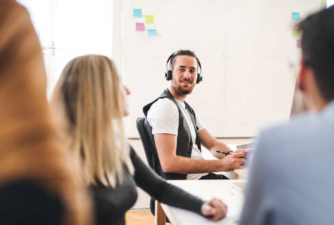 Ein Porträt eines jungen Geschäftsmannes mit Kopfhörern und Kollegen in einem modernen Büro. - HPIF27879