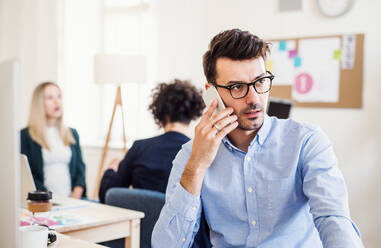 Junger Geschäftsmann mit Smartphone, der in einem modernen Büro arbeitet und einen Anruf tätigt. - HPIF27888