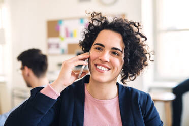 Ein Porträt einer jungen Geschäftsfrau mit Smartphone in einem modernen Büro, die einen Anruf tätigt. - HPIF27894