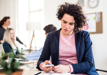 Porträt einer jungen Geschäftsfrau mit Smartphone in einem modernen Büro, Textnachrichten. - HPIF27895