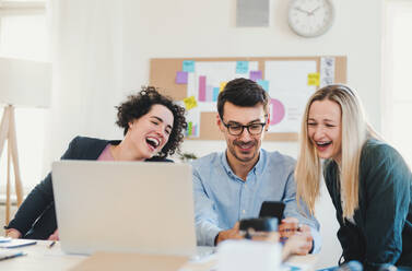 Eine Gruppe junger, fröhlicher Geschäftsleute mit Laptop arbeitet in einem modernen Büro zusammen. - HPIF27903