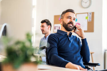 Junger Geschäftsmann im Rollstuhl mit Smartphone bei der Arbeit in einem modernen Büro, der einen Anruf tätigt. - HPIF27908