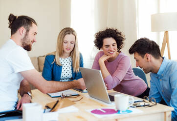 Group of young concentrated male and female businesspeople with laptop sitting at the table, working in a modern office. - HPIF27910