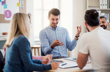 Eine Gruppe junger, fröhlicher Geschäftsleute sitzt in einem modernen Büro um einen Tisch herum und hält eine Besprechung ab. - HPIF27912