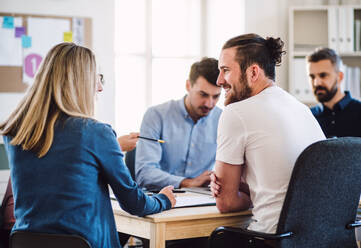 Eine Gruppe junger, fröhlicher Geschäftsleute sitzt in einem modernen Büro um einen Tisch herum und hält eine Besprechung ab. - HPIF27915