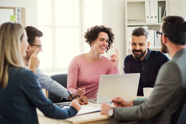 Group of young, cheerful businesspeople sitting around table in a modern office, having meeting. - HPIF27918