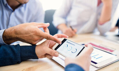 Group of young, male and female businesspeople with smartphone and tablet working together in a modern office, a midsection view. - HPIF27926