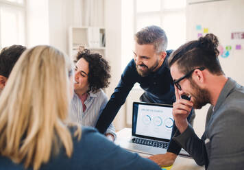 Eine Gruppe junger, fröhlicher Geschäftsleute mit Laptop arbeitet in einem modernen Büro zusammen. - HPIF27929