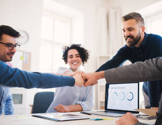 Group of young businesspeople sitting around table in a modern office, making fist bump. - HPIF27931