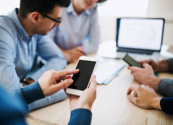 A midsection of group of young businesspeople with smartphone having meeting in office. Copy space. - HPIF27935