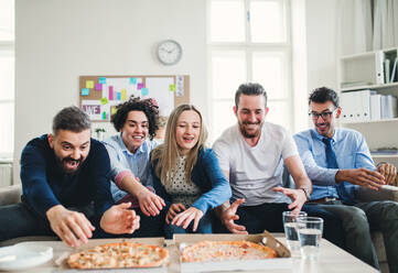 Eine Gruppe von jungen Geschäftsleuten mit Pizza beim Mittagessen in einem modernen Büro. - HPIF27946