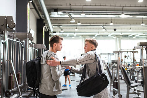 Junge männliche Freunde mit Taschen im modernen Crossfit-Fitnessstudio, die sich gegenseitig begrüßen. - HPIF27951