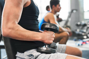 Unbekannte junge, fitte Männer beim Krafttraining, die mit Hanteln in einem modernen Fitnessstudio trainieren. - HPIF27961