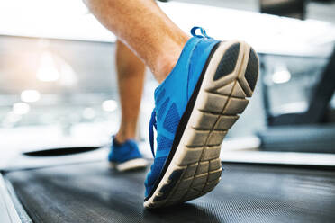 Nahaufnahme der Füße eines jungen Mannes im Fitnessstudio beim Laufen auf dem Laufband. - HPIF27969