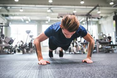 Ein fitter Mann macht Krafttraining, macht Liegestütze in einem modernen Fitnessstudio. - HPIF27971