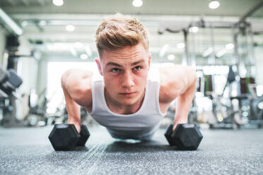 Fit man doing strength training, doing push ups on dumbbells in modern gym. Close-up. - HPIF27972