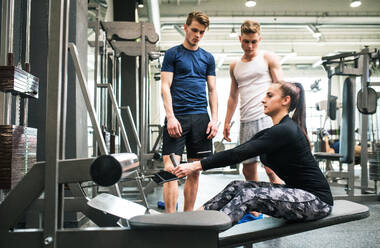 Junge Männer in einem Fitnessstudio schauen auf einen Personal Trainer, der an einer Kabelgewichtsmaschine trainiert. - HPIF27977
