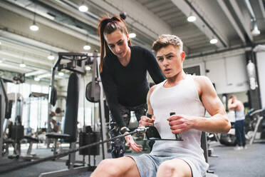 Fit junger Mann im Fitnessstudio mit seinem persönlichen Trainer arbeiten auf Kabel Gewicht Maschine. - HPIF27979