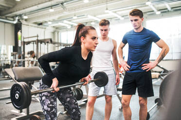 Junge, gut aussehende, fitte Männer im Fitnessstudio, die ihren Personal Trainer beim Training beobachten, eine Hantelstange heben und ihre Muskeln anspannen. - HPIF27982