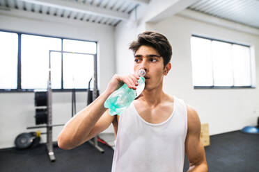 Junger, gut aussehender, fitter Mann im Fitnessstudio, ruht sich zwischen den Übungen aus und trinkt Wasser. - HPIF27984