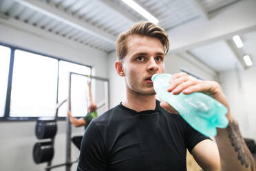 Junger, gut aussehender, fitter Mann im Fitnessstudio, ruht sich zwischen den Übungen aus und trinkt Wasser. - HPIF27985