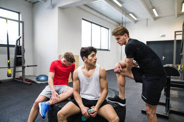 Three young fit men in crossfit gym resting after an exercise, talking. - HPIF27990