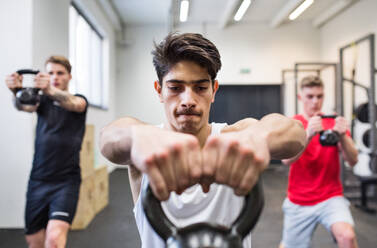Three young fit men in crossfit gym working out, doing kettlebell swings. - HPIF27999