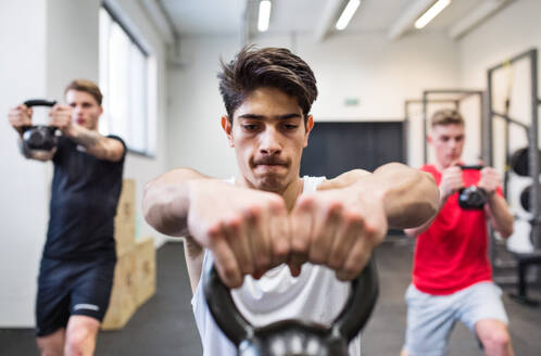 Drei junge, fitte Männer trainieren im Crossfit-Fitnessstudio und machen Kettlebell-Schwünge. - HPIF27999