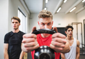 Drei junge, fitte Männer trainieren im Crossfit-Fitnessstudio und machen Kettlebell-Schwünge. - HPIF28000