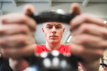 Fit hispanic man doing strength training, lifting kettlebell in crossfit gym. Close-up. - HPIF28001