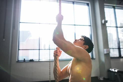 A fit young man in gym standing topless , holding a climbing rope. Copy space. - HPIF28019