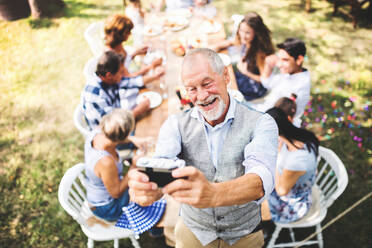 Mehrgenerationen-Party im Garten: Opa hält den Moment mit einem Selfie-Stick bei der großen Gartenparty fest - HPIF28070