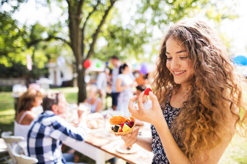 Family celebration outside in the backyard. Big garden party. A teenage girl eating fruit. - HPIF28086