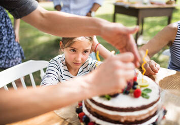 Familienfeier draußen im Garten. Große Gartenparty. Geburtstagsparty. Kleines Mädchen mit Geburtstagstorte. - HPIF28093