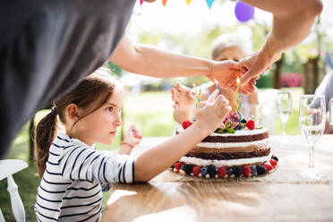 Familienfeier draußen im Garten. Große Gartenparty. Geburtstagsparty. Kleines Mädchen mit Geburtstagstorte. - HPIF28094