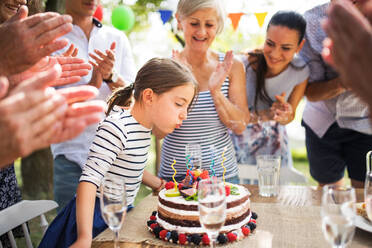 Familienfeier draußen im Garten. Große Gartenparty. Geburtstagsparty. Kleines Mädchen mit Geburtstagstorte. - HPIF28095