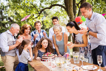 Familienfeier draußen im Garten. Große Gartenparty. Geburtstagsfeier. Ein Teenager-Mädchen mit einer Geburtstagstorte. - HPIF28097