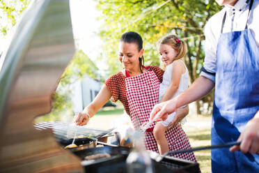 Familienfeier im Hinterhof, Grillparty, eine Frau mit einem kleinen Mädchen im Arm und ein nicht erkennbarer Mann beim Kochen. - HPIF28115