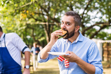 Family celebration outside in the backyard. Barbecue party. A mature man eating hamburger. - HPIF28118