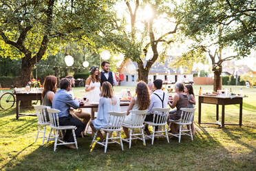 Hochzeitsempfang im Hinterhof. Der gutaussehende Bräutigam hält eine Rede. Die Gäste sitzen um den Tisch herum. - HPIF28122