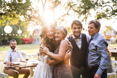 Hochzeitsempfang im Hinterhof, Familienfeier, Braut, Bräutigam und Eltern posieren bei Sonnenuntergang für ein Foto. - HPIF28129