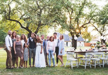 Wedding reception outside in the backyard. Family celebration. Bride, groom and their guests posing for the photo. - HPIF28137