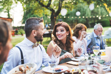 Die Gäste sitzen am Tisch und essen bei der Hochzeitsfeier draußen im Garten. - HPIF28139