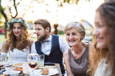 Hochzeitsempfang im Hinterhof, Braut, Bräutigam und Gäste sitzen am Tisch. - HPIF28142