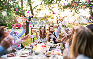 Hochzeitsempfang im Hinterhof: Braut und Bräutigam mit Familie und Gästen, die am Tisch sitzen und Spaß haben. - HPIF28143